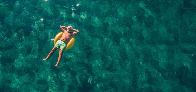 An older man relaxing and laying down in an inner tube on relaxing water.