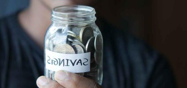 Person holding jar of coins with a 'savings' label